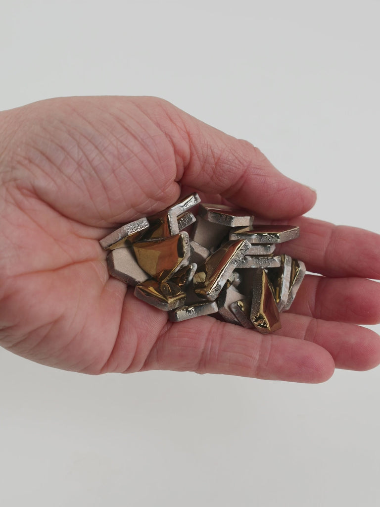 Video of Flip ceramic puzzle pieces in gold, opaque glazed porcelain, 4–20 mm, held in a hand and poured out to show their shapes and finish