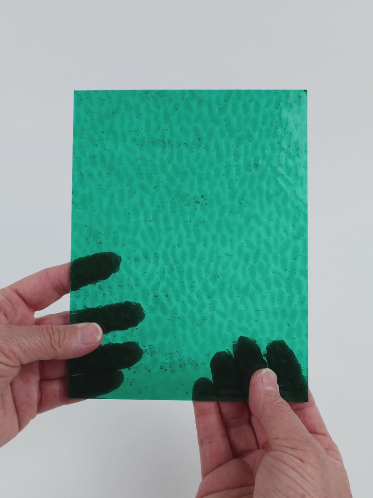 Video of the Teal Hammered glass plate in hammered transparent teal, 15x19cm, held up and tilted to show its pattern and transparency