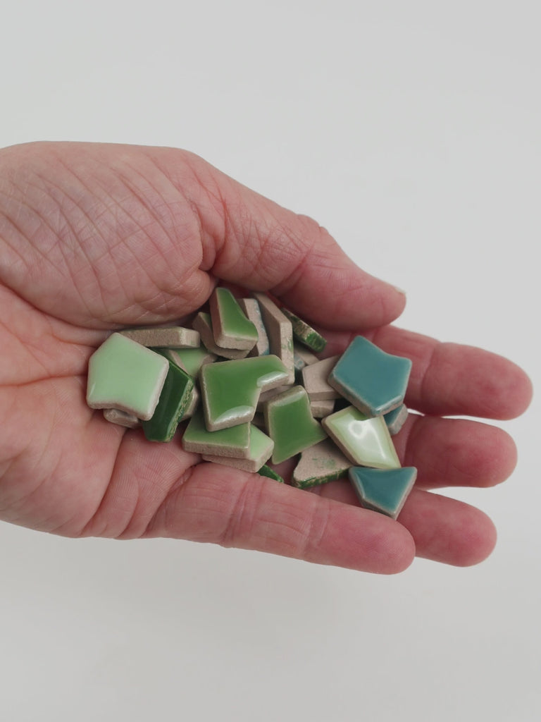 Video of Flip ceramic puzzle pieces in green mix, opaque glazed porcelain, 4–20 mm, held in a hand and poured out to show their shapes and finish