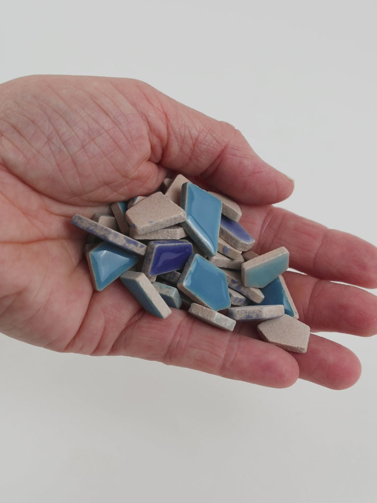 Video of Flip ceramic puzzle pieces in blue mix, opaque glazed porcelain, 4–20 mm, held in a hand and poured out to show their shapes and finish