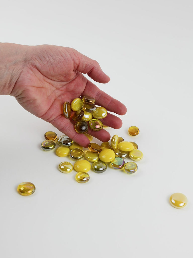 Video of yellow mix glass nuggets in lemon, golden and amber shades with an iridescent sheen, 16–20 mm, picked up from a pile by hand and dropped back to show their size, round shape and shine