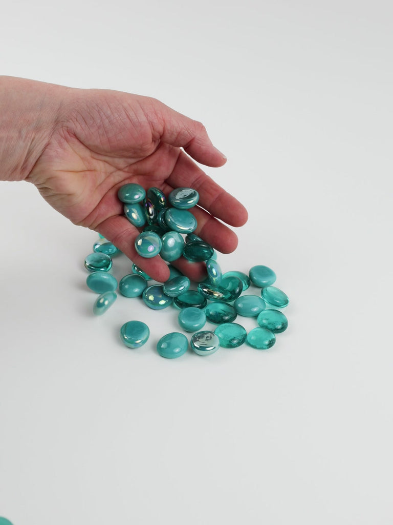 Video of green-blue mix glass nuggets in teal and aqua shades with an iridescent sheen, 16–20 mm, picked up from a pile by hand and dropped back to show their size, round shape and shine