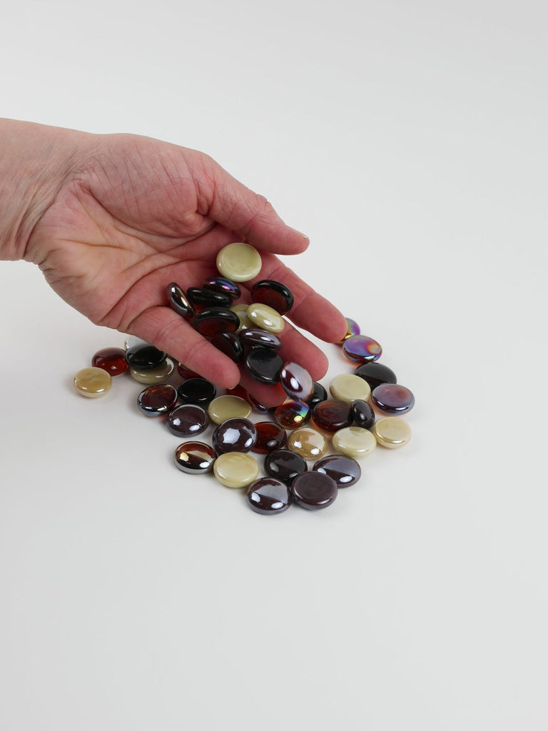 Video of caramel mix glass nuggets in dark brown, amber and cream shades with an iridescent sheen, 16–20 mm, picked up from a pile by hand and dropped back to show their size, round shape and shine