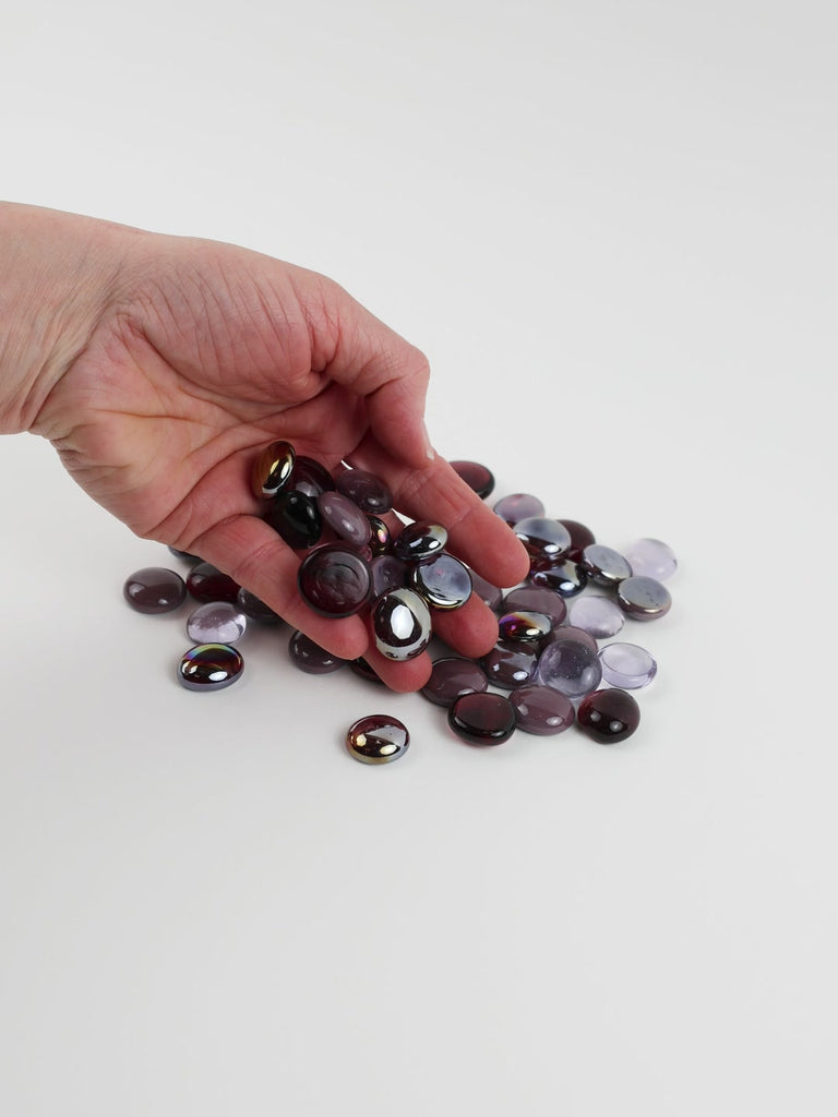 Video of purple mix glass nuggets in aubergine, plum and lilac shades with an iridescent sheen, 16–20 mm, picked up from a pile by hand and dropped back to show their size, round shape and shine
