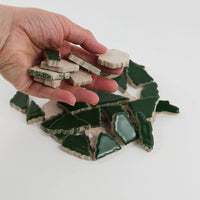 Video of Flip XL ceramic puzzle pieces in moss green, opaque glazed porcelain, 20–60 mm, picked up from a pile by hand and dropped back to show their size, shapes and finish