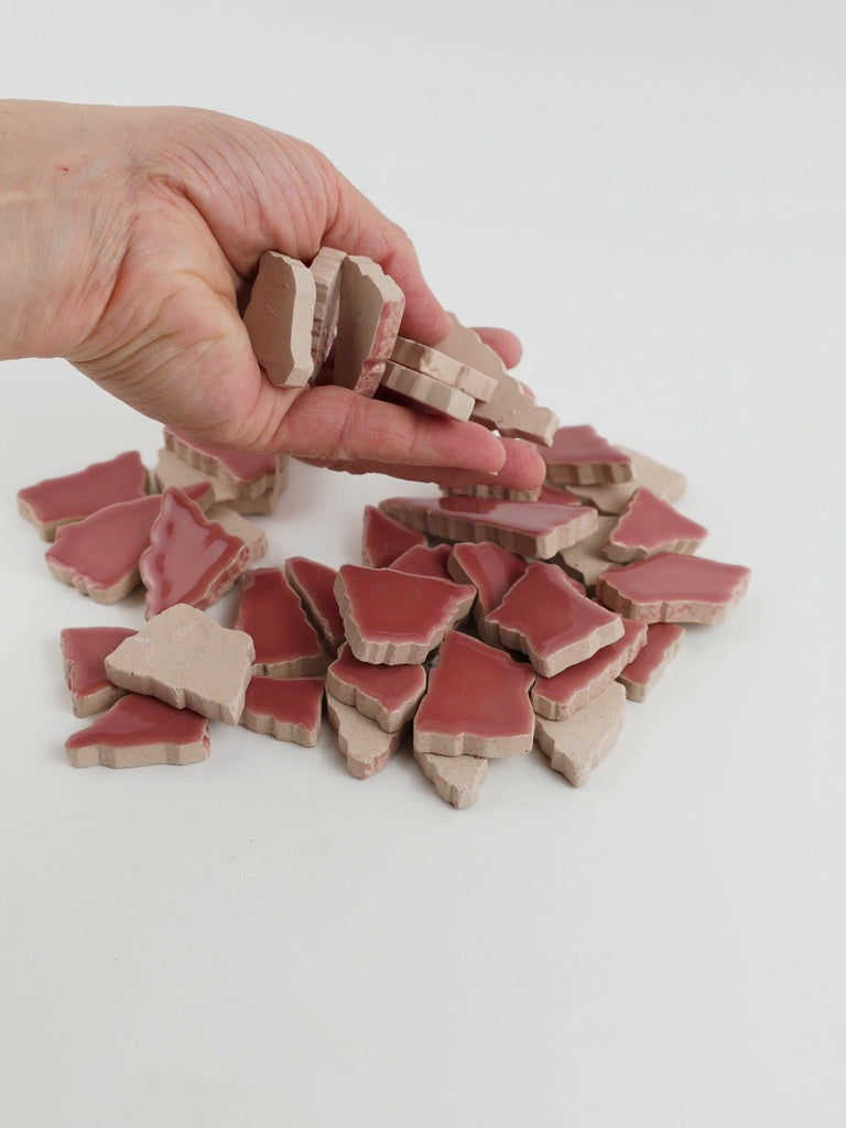 Video of Flip XL ceramic puzzle pieces in light pink, opaque glazed porcelain, 20–60 mm, picked up from a pile by hand and dropped back to show their size, shapes and finish