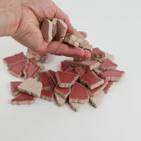 Video of Flip XL ceramic puzzle pieces in light pink, opaque glazed porcelain, 20–60 mm, picked up from a pile by hand and dropped back to show their size, shapes and finish