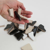 Video of Flip XL ceramic puzzle pieces in grey mix, opaque glazed porcelain, 20–60 mm, picked up from a pile by hand and dropped back to show their size, shapes and finish