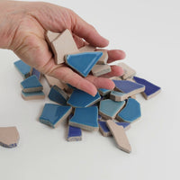 Video of Flip XL ceramic puzzle pieces in blue mix, opaque glazed porcelain, 20–60 mm, picked up from a pile by hand and dropped back to show their size, shapes and finish