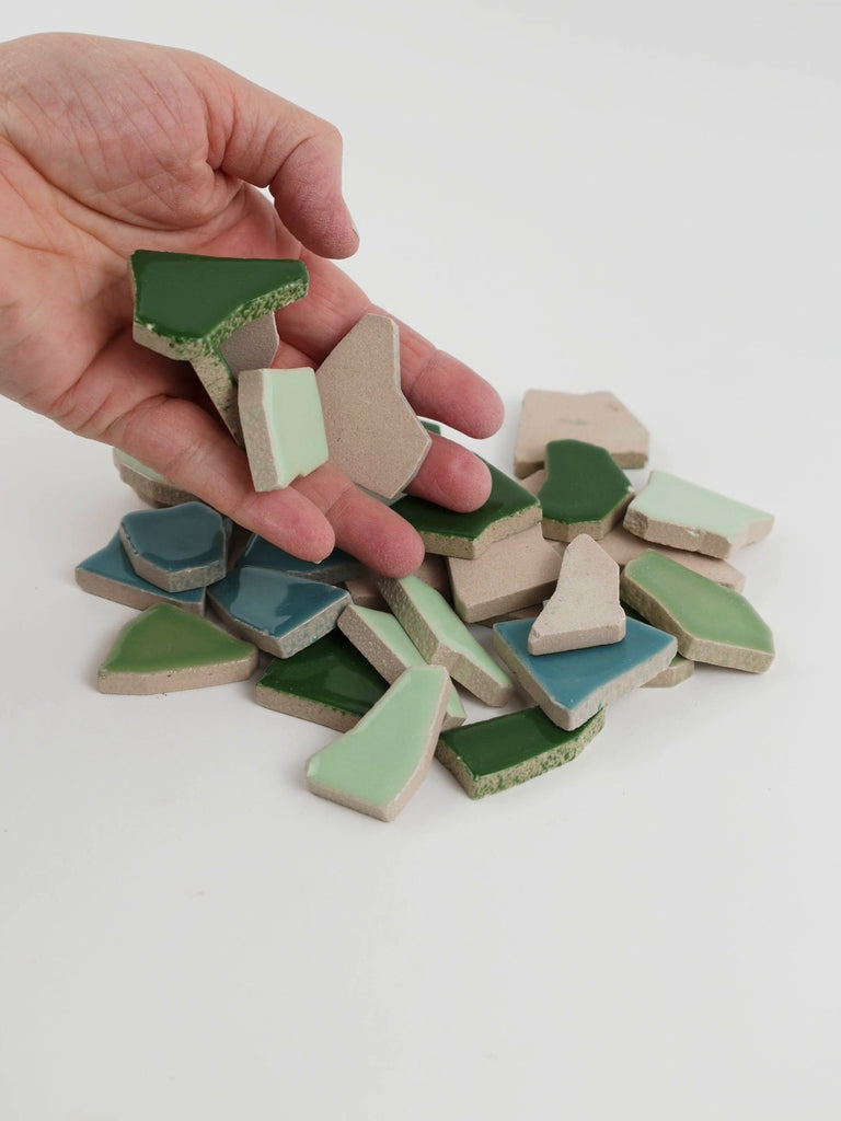 Video of Flip XL ceramic puzzle pieces in green mix, opaque glazed porcelain, 20–60 mm, picked up from a pile by hand and dropped back to show their size, shapes and finish