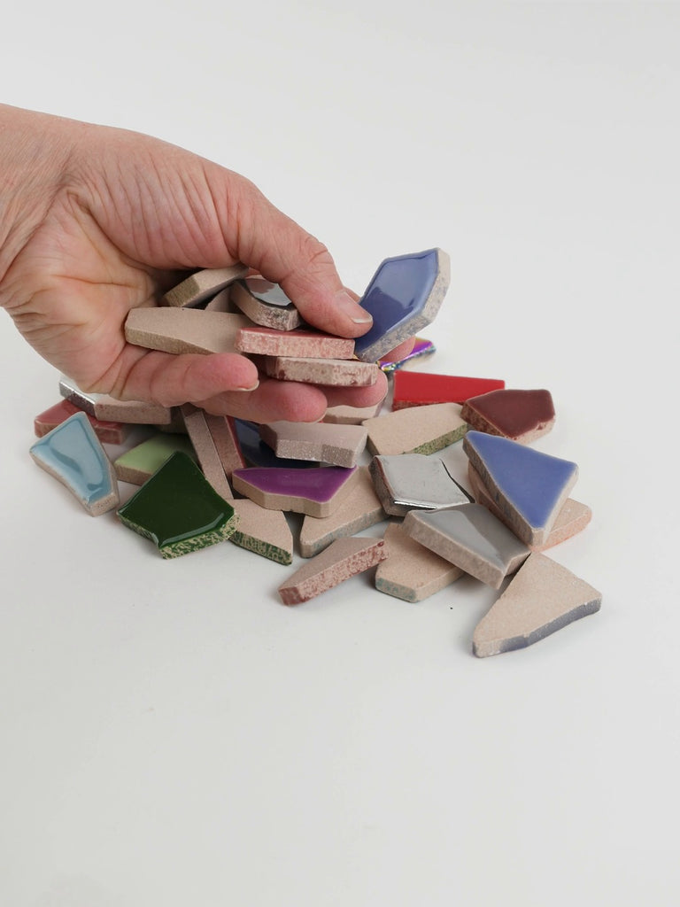 Video of Flip XL ceramic puzzle pieces in tropical mix, opaque glazed porcelain, 20–60 mm, picked up from a pile by hand and dropped back to show their size, shapes and finish
