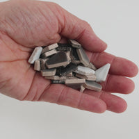 Video of Flip ceramic puzzle pieces in grey mix, opaque glazed porcelain, 4–20 mm, held in a hand and poured out to show their shapes and finish
