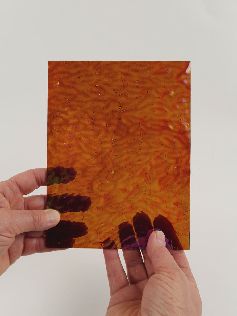 Video of the Amber Hammered iridescent glass plate in transparant amber, 15x19cm, held up and tilted to show its pattern and transparency