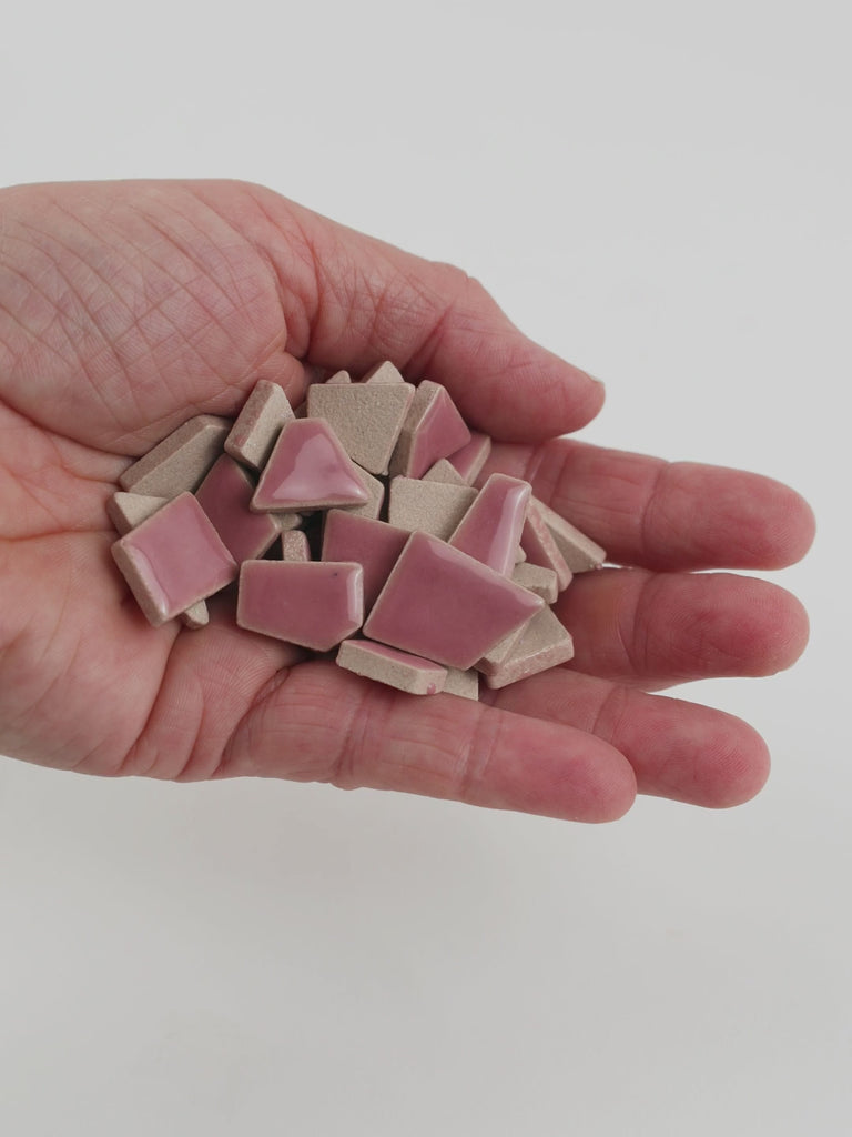 Video of Flip ceramic puzzle pieces in light pink, opaque glazed porcelain, 4–20 mm, held in a hand and poured out to show their shapes and finish